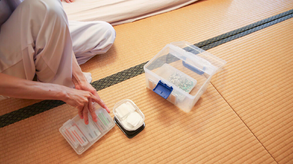 畳の部屋で使い捨て鍼や消毒綿など訪問鍼灸の道具を準備する様子