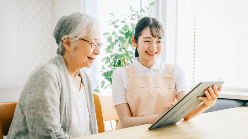 タブレットを見せながら説明するケアマネージャーと話を聞く高齢女性